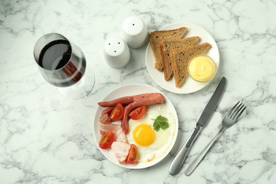 Photo of Tasty brunch. Fried egg, sausage, bacon and tomatoes served with wine on white marble table, flat lay