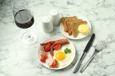 Photo of Tasty brunch. Fried egg, sausage, bacon and tomatoes served with wine on white marble table