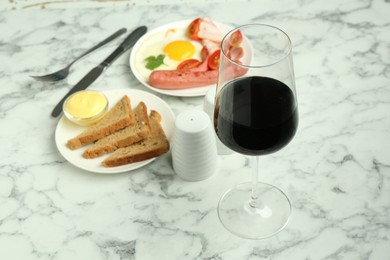 Photo of Tasty brunch. Glass of red wine, fried egg, sausage, bread and sauce on white marble table