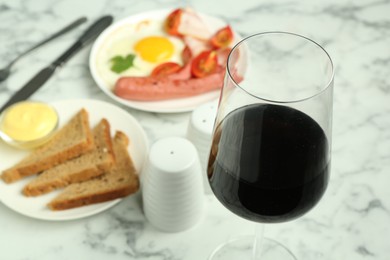 Photo of Tasty brunch. Glass of red wine, fried egg, sausage, bread and sauce on white marble table, closeup