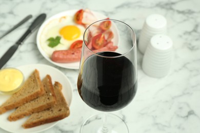 Photo of Tasty brunch. Glass of red wine, fried egg, sausage, bread and sauce on white marble table, closeup