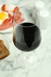 Photo of Tasty brunch. Glass of red wine, fried egg and sausage on white marble table, closeup