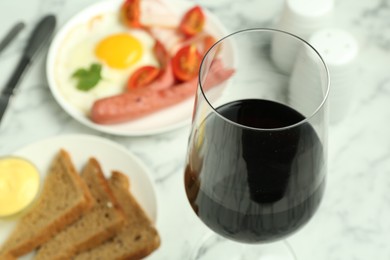 Photo of Tasty brunch. Glass of red wine, fried egg, sausage, bread and sauce on white marble table, closeup