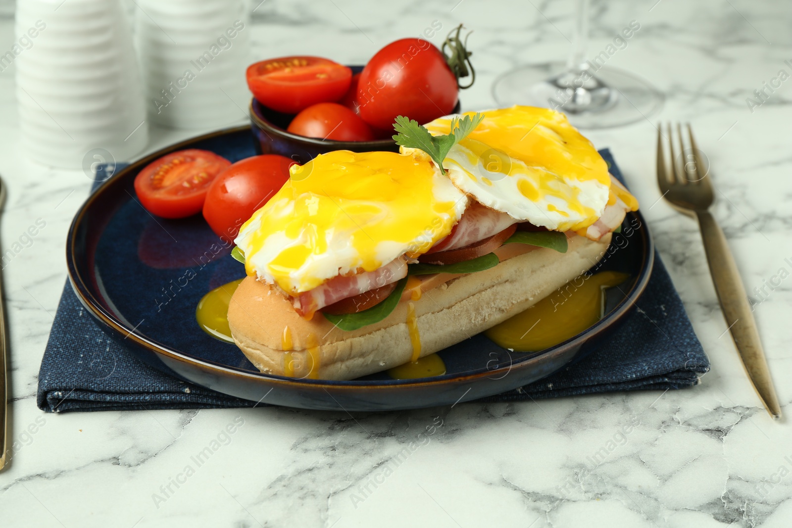 Photo of Tasty brunch. Poached eggs, bacon, bun and tomatoes served on white marble table, closeup