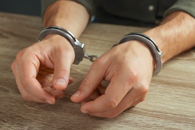 Photo of Man in metal handcuffs at wooden table, closeup