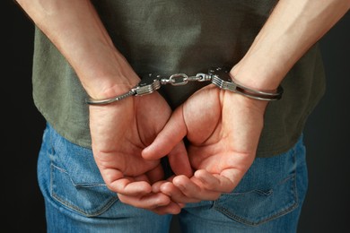 Photo of Man in metal handcuffs on black background, back view