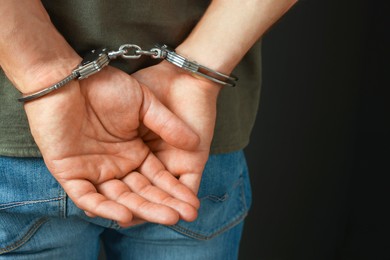 Photo of Man in metal handcuffs on black background, closeup