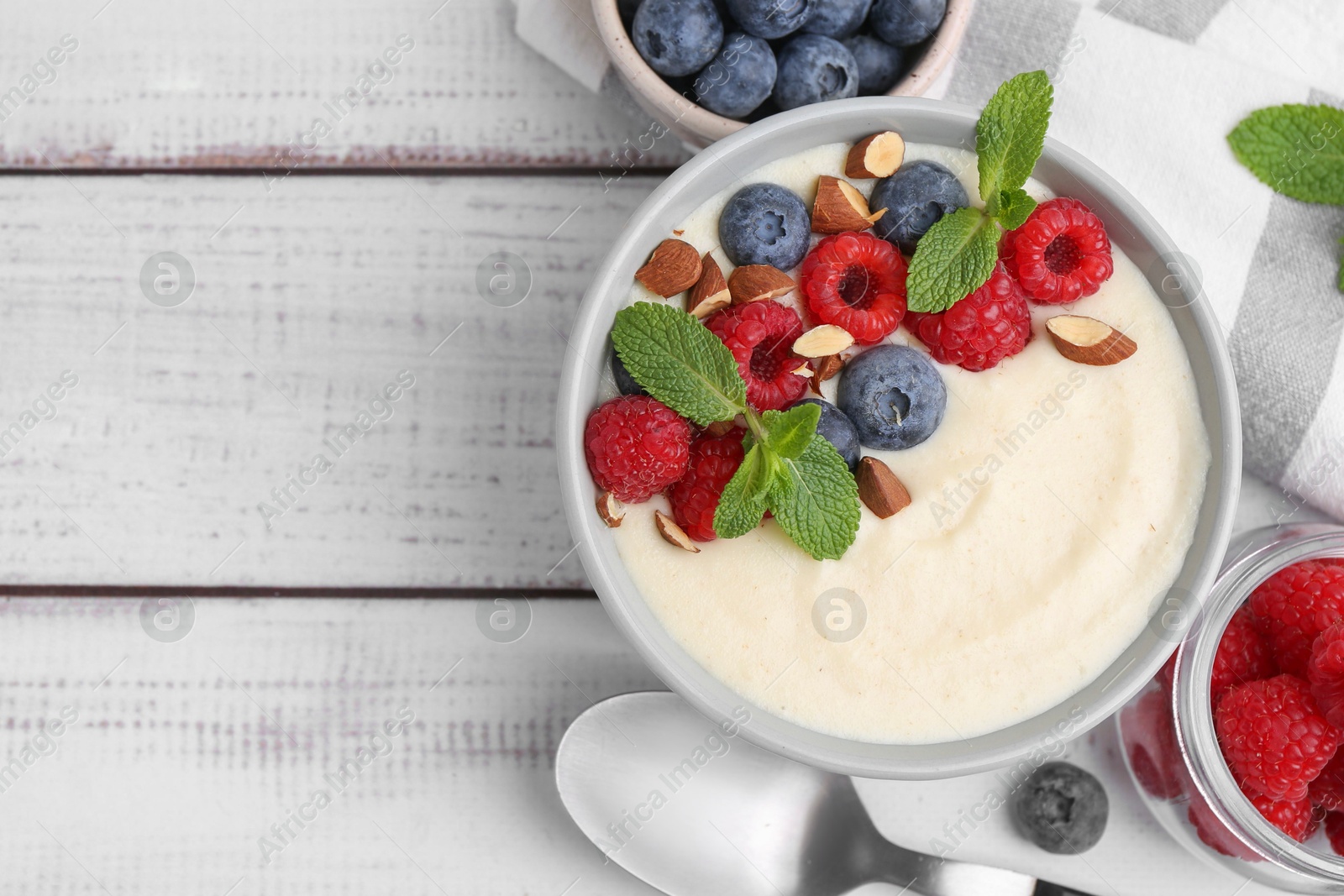 Photo of Tasty cooked semolina porridge with almonds, berries and mint on white wooden table, top view. Space for text