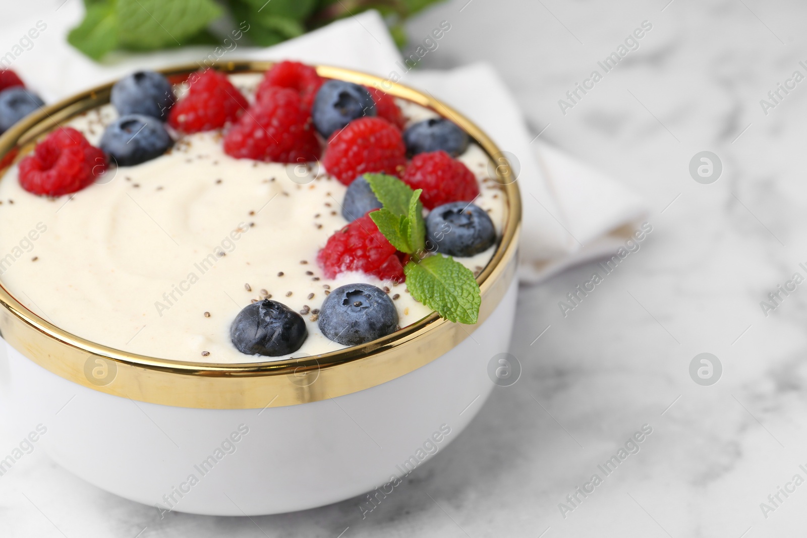 Photo of Tasty cooked semolina porridge with berries and mint on white marble table, closeup. Space for text