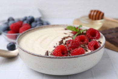 Photo of Tasty cooked semolina porridge with raspberries, chocolate and mint on white table, closeup