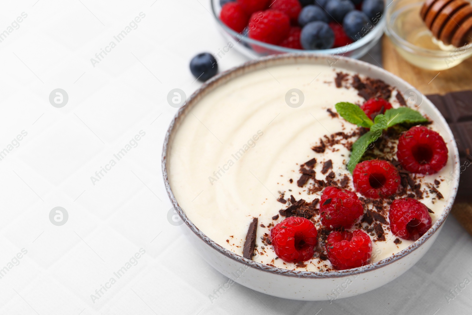 Photo of Tasty cooked semolina porridge with berries served on white tiled table, closeup. Space for text