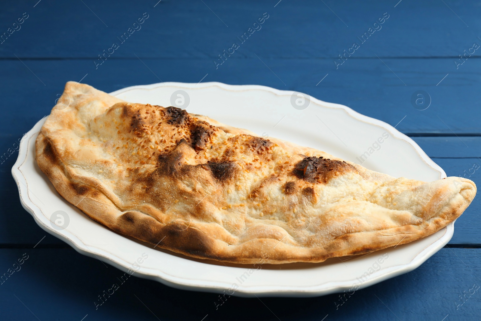 Photo of Plate with tasty calzone on blue wooden table, closeup