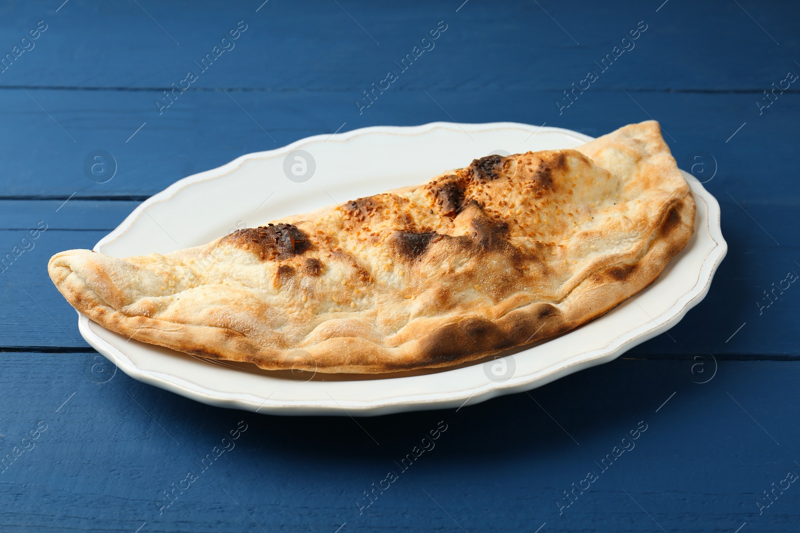 Photo of Plate with tasty calzone on blue wooden table, closeup