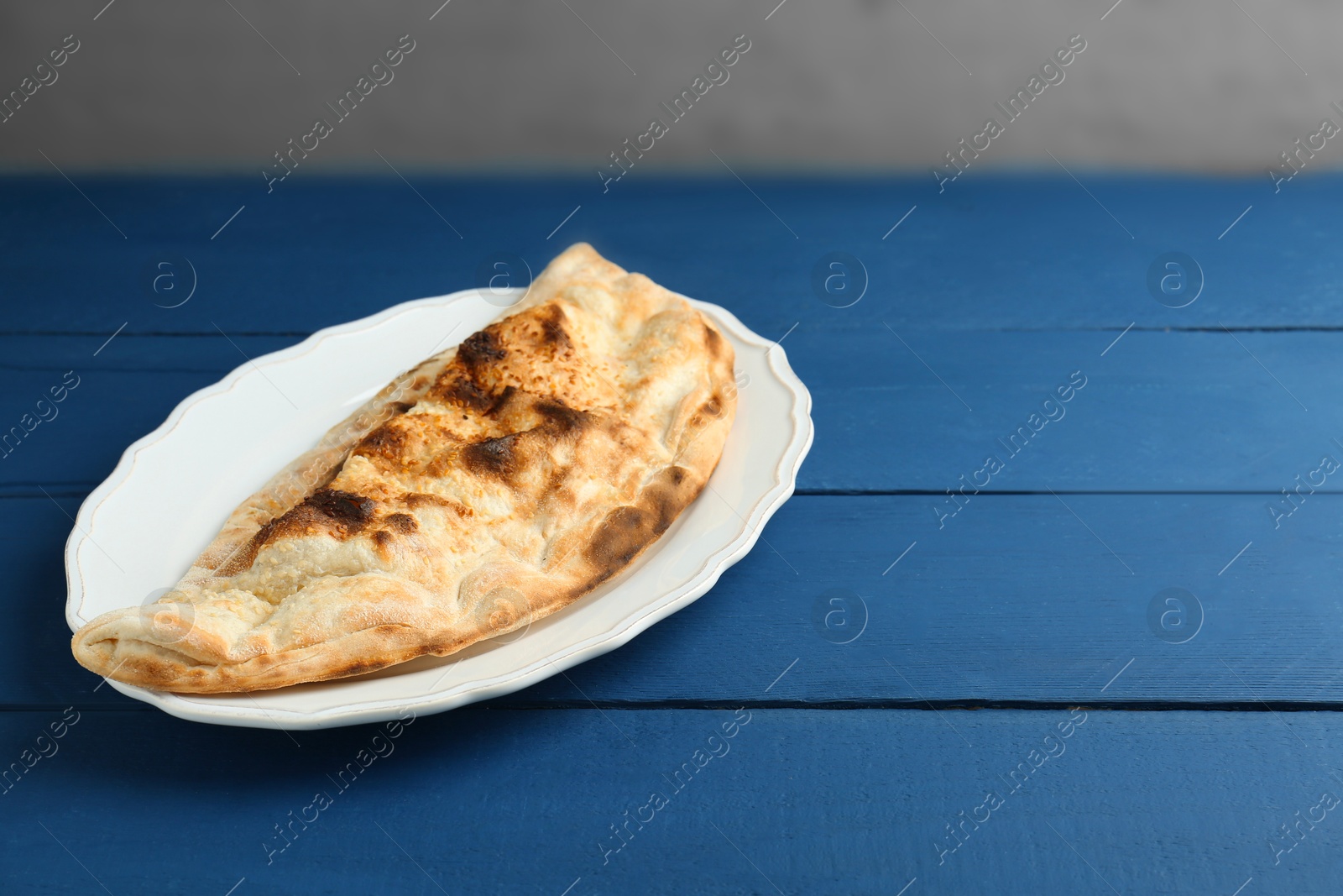 Photo of Plate with tasty calzone on blue wooden table. Space for text