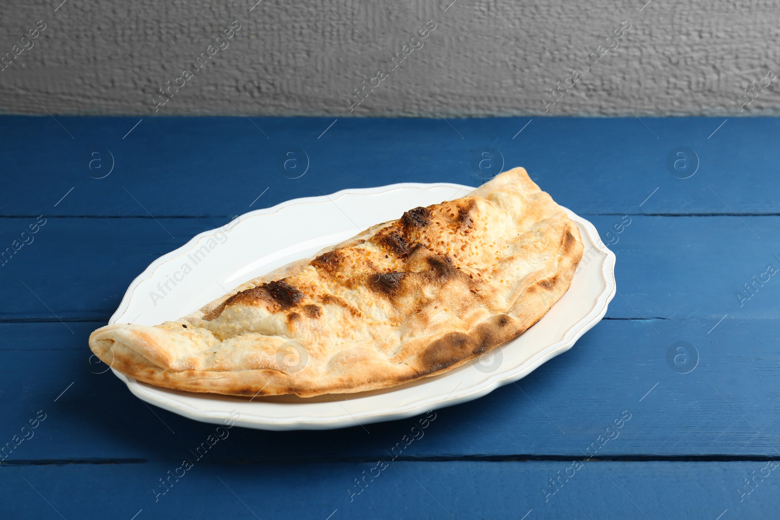 Photo of Plate with tasty calzone on blue wooden table