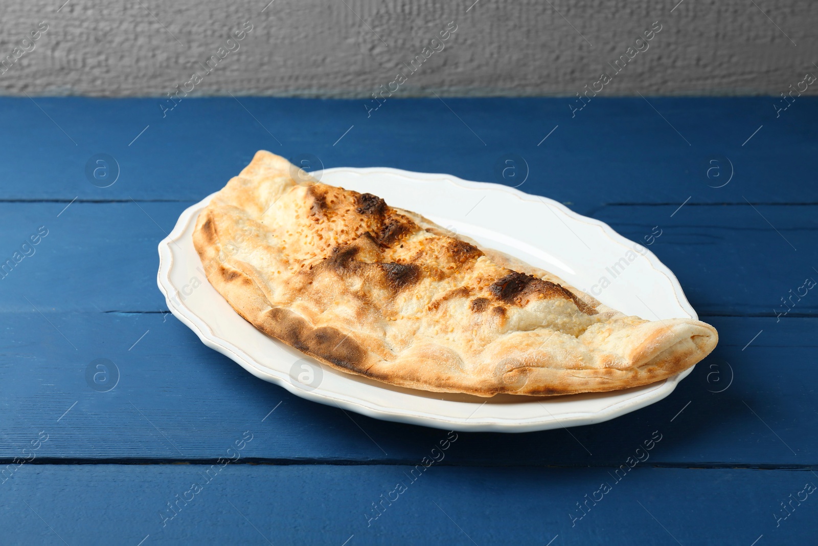 Photo of Plate with tasty calzone on blue wooden table