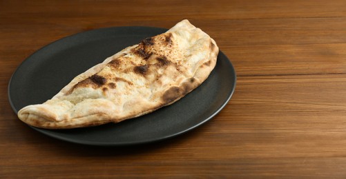 Photo of Plate with tasty calzone on wooden table, closeup. Space for text