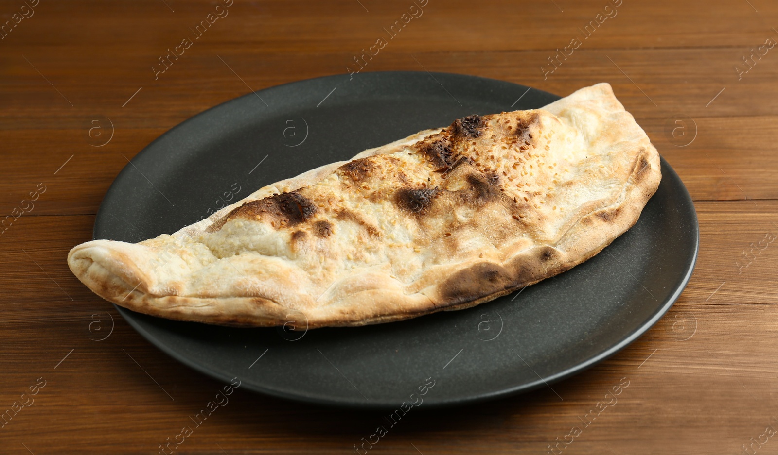 Photo of Plate with tasty calzone on wooden table, closeup