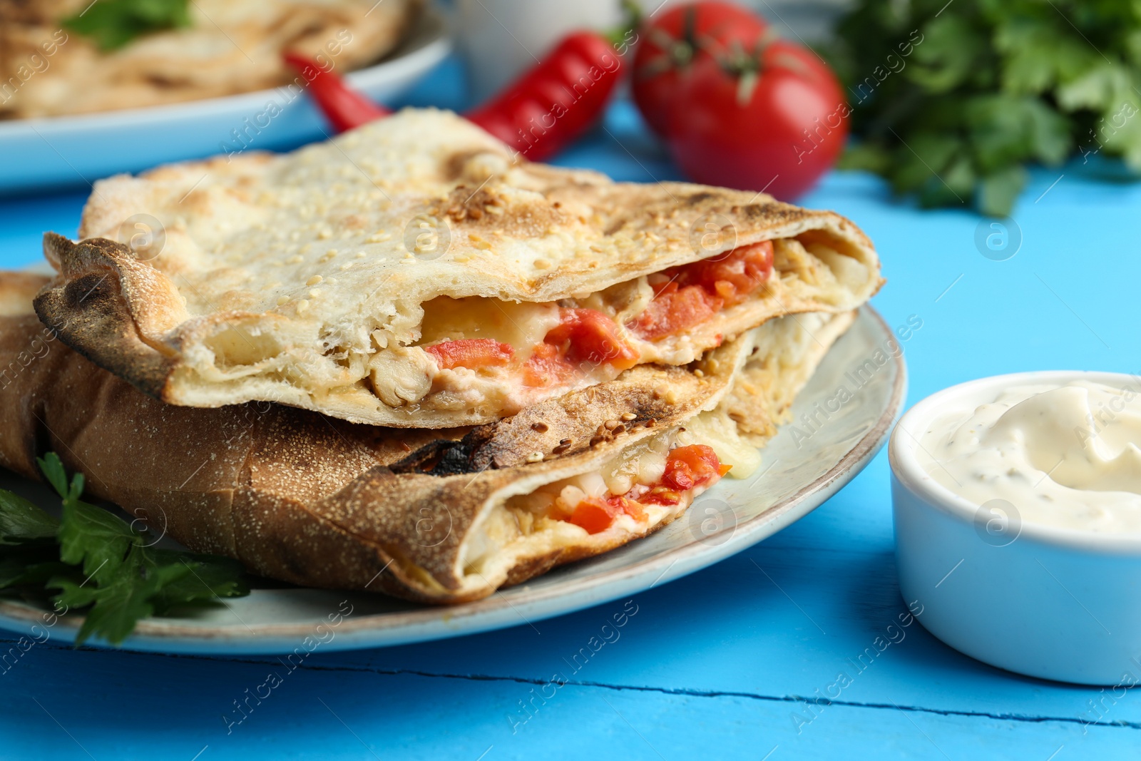 Photo of Halves of tasty calzone with meat, cheese, tomato and sauce on light blue table, closeup