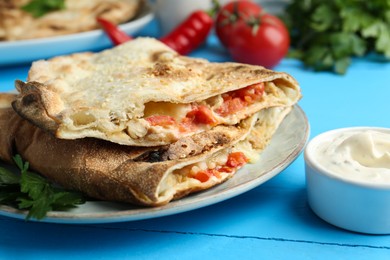 Photo of Halves of tasty calzone with meat, cheese, tomato and sauce on light blue table, closeup