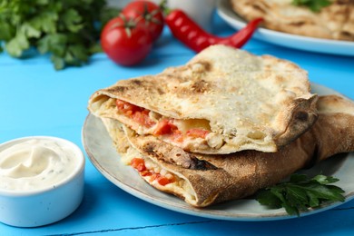 Photo of Halves of tasty calzone with meat, cheese, tomato and sauce on light blue table, closeup