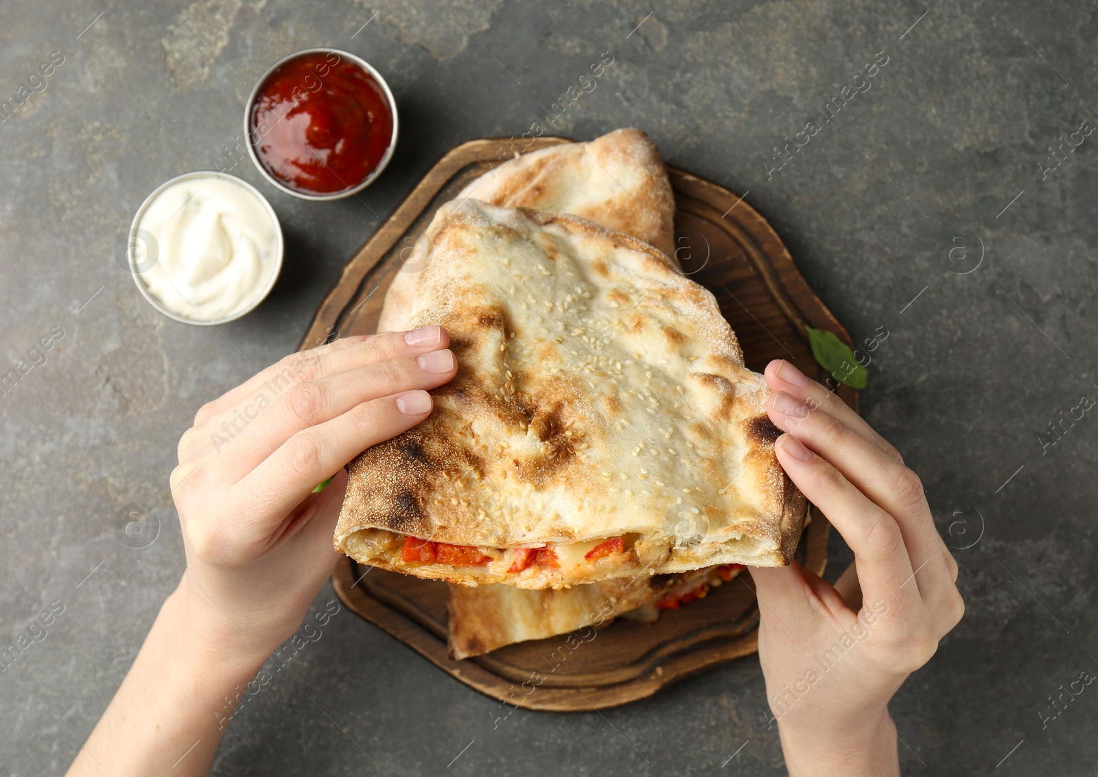 Photo of Woman eating tasty calzone with meat, cheese and tomato at grey textured table, top view