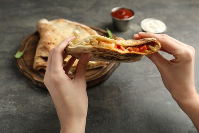 Photo of Woman eating tasty calzone with meat, cheese and tomato at grey textured table, closeup