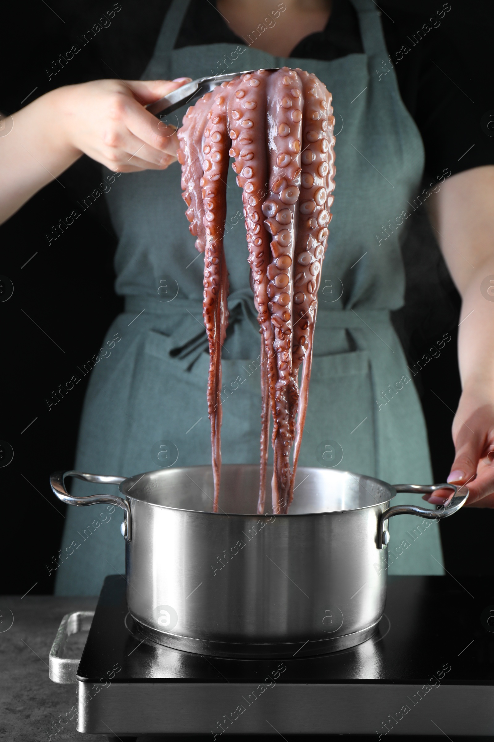 Photo of Woman taking boiled octopus from pan on stove, closeup