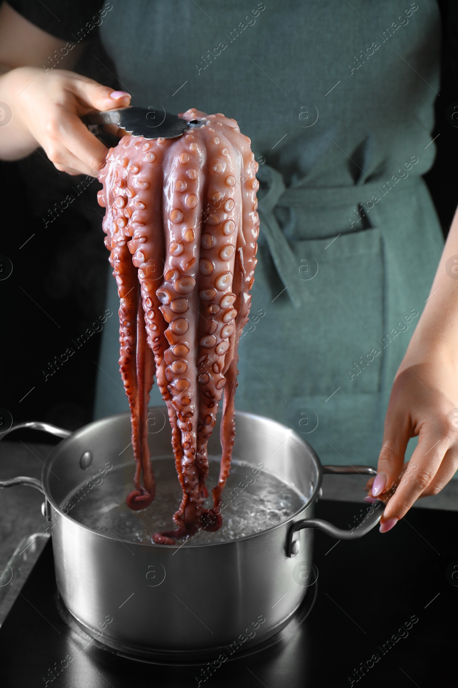 Photo of Woman taking boiled octopus from pan on stove, closeup