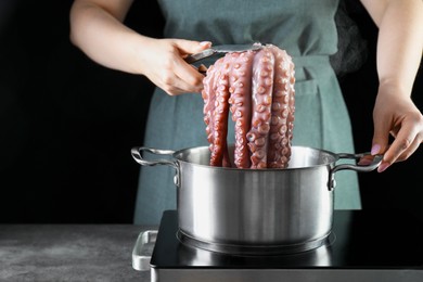 Photo of Woman taking boiled octopus from pan on stove, closeup