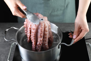 Photo of Woman taking boiled octopus from pan on stove, closeup