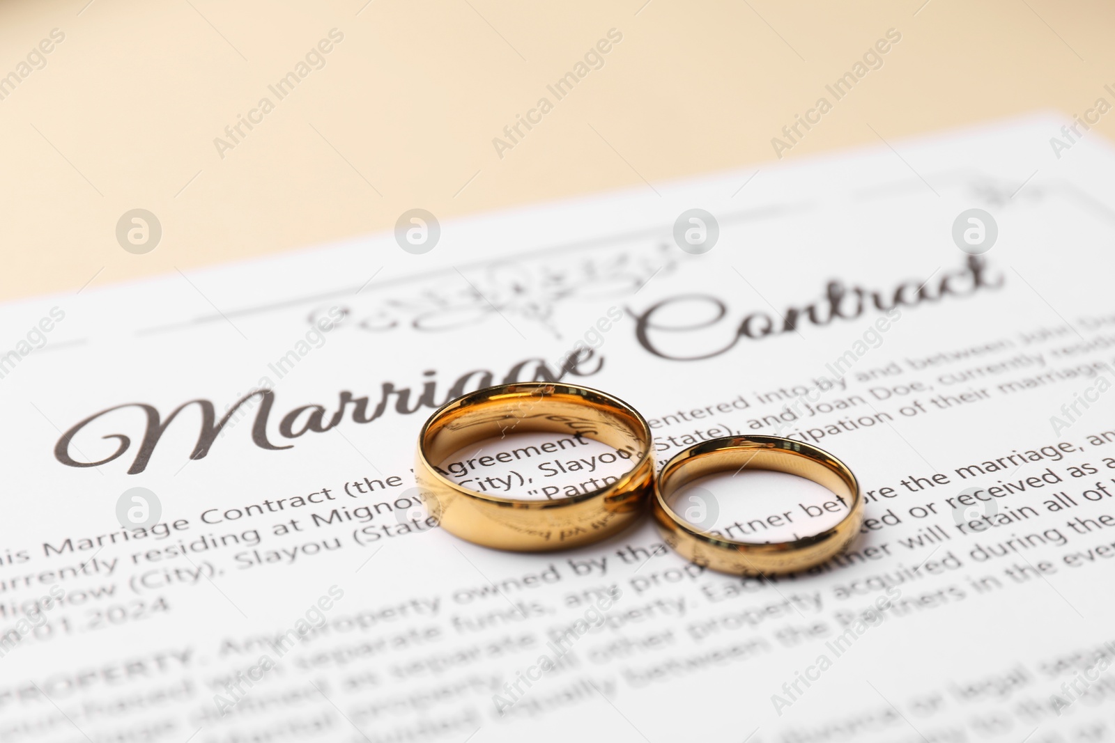 Photo of Marriage contract and golden rings on beige background, closeup