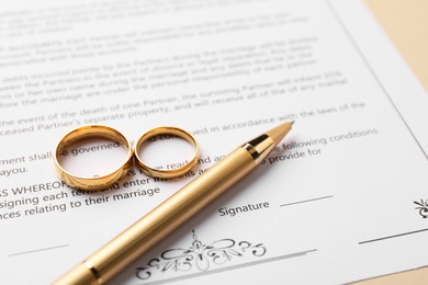 Photo of Marriage contract, pen and golden rings on beige background, closeup