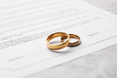 Photo of Marriage contract and golden rings on white marble table, closeup