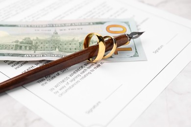 Photo of Marriage contract, dollar bill, pen and golden rings on white marble table, closeup