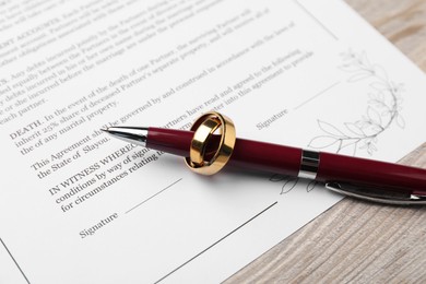 Photo of Marriage contract, pen and golden ring on light wooden table, closeup