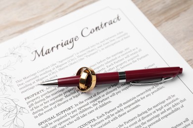 Photo of Marriage contract, pen and golden ring on light wooden table, above view