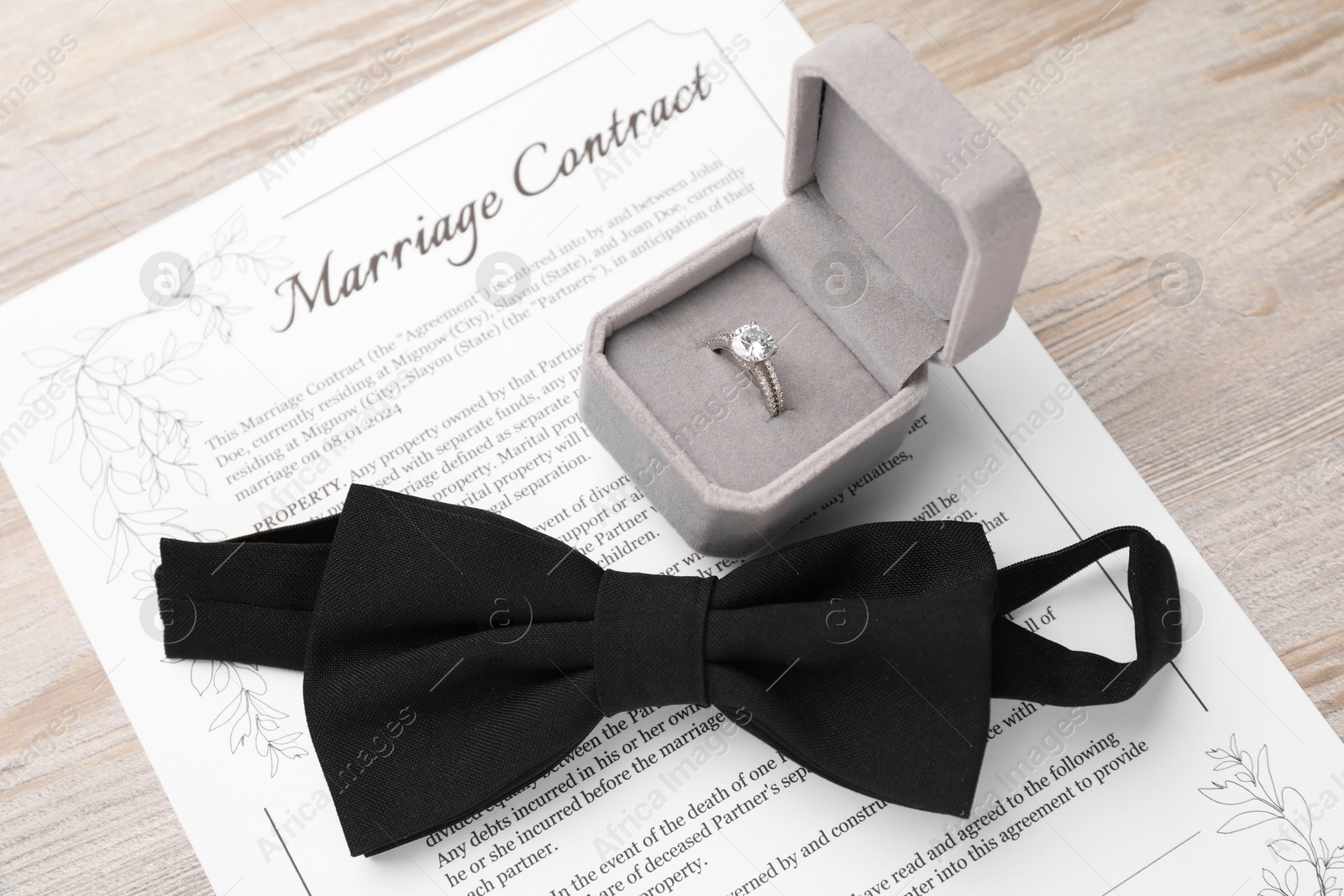 Photo of Marriage contract, bowtie and ring on light wooden table, above view