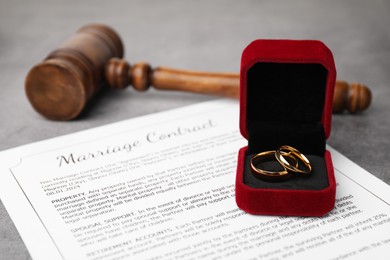 Photo of Marriage contract, gavel and golden rings on grey table, closeup