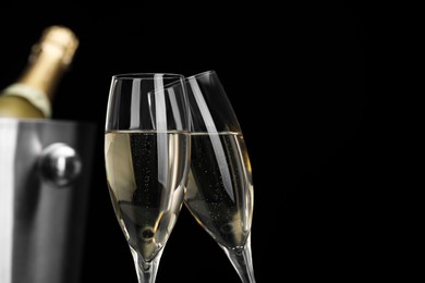 Photo of Champagne in glasses and ice bucket with bottle on black background, space for text