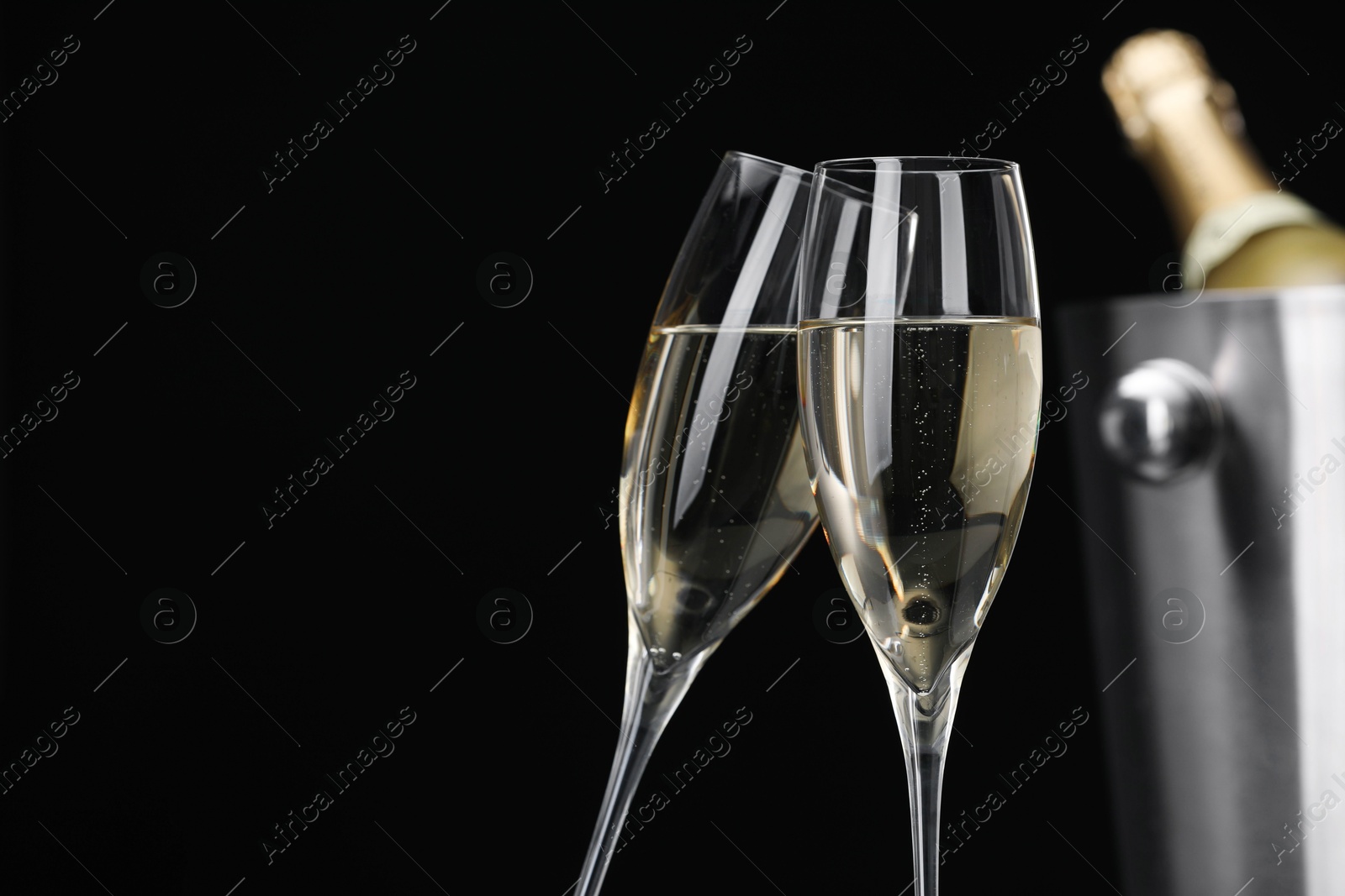 Photo of Champagne in glasses and ice bucket with bottle on black background, space for text