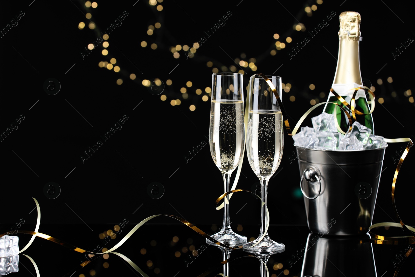 Photo of Champagne and bucket of ice on mirror surface against black background with blurred lights, space for text