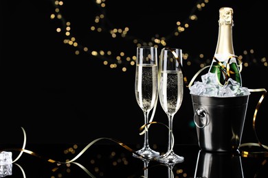 Photo of Champagne and bucket of ice on mirror surface against black background with blurred lights, space for text