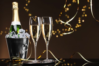 Photo of Champagne and bucket of ice on mirror surface against brown background with blurred lights, space for text