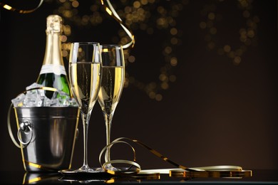 Photo of Champagne and bucket of ice on mirror surface against brown background with blurred lights, space for text