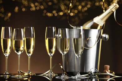 Photo of Champagne in glasses and ice bucket with bottle on mirror surface against brown background with blurred lights