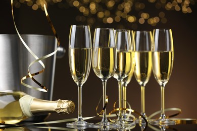 Photo of Champagne in glasses and bottle on mirror surface against brown background with blurred lights