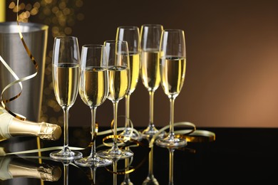 Photo of Champagne in glasses and bottle on mirror surface against brown background with blurred lights, space for text