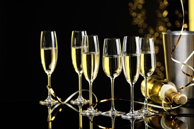 Photo of Champagne in glasses and bottle on mirror surface against black background with blurred lights