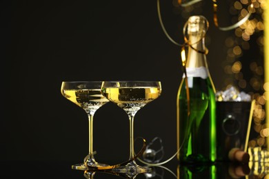 Photo of Champagne in glasses and ice bucket with bottle on mirror surface against black background with blurred lights